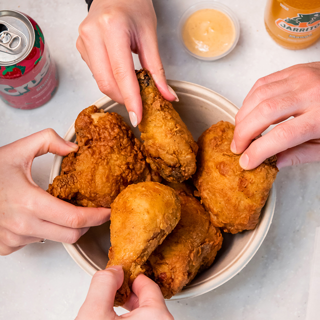 hands grab pieces of fried chicken from a communal bowl